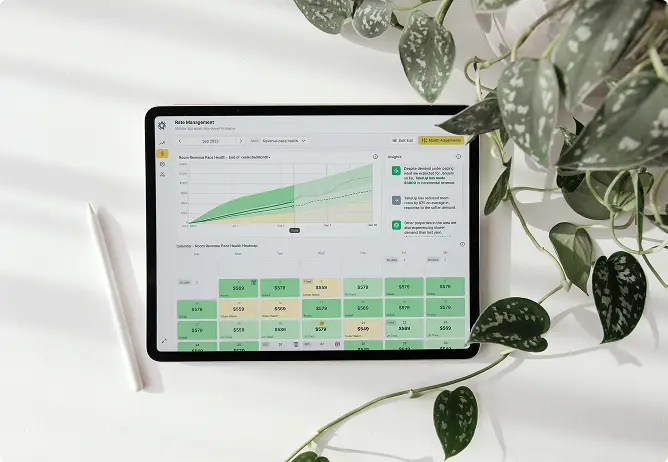 A tablet on a white desk displays a hotel's dynamic pricing dashboard, featuring a revenue graph, an AI insights panel, and a calendar of future room rates.